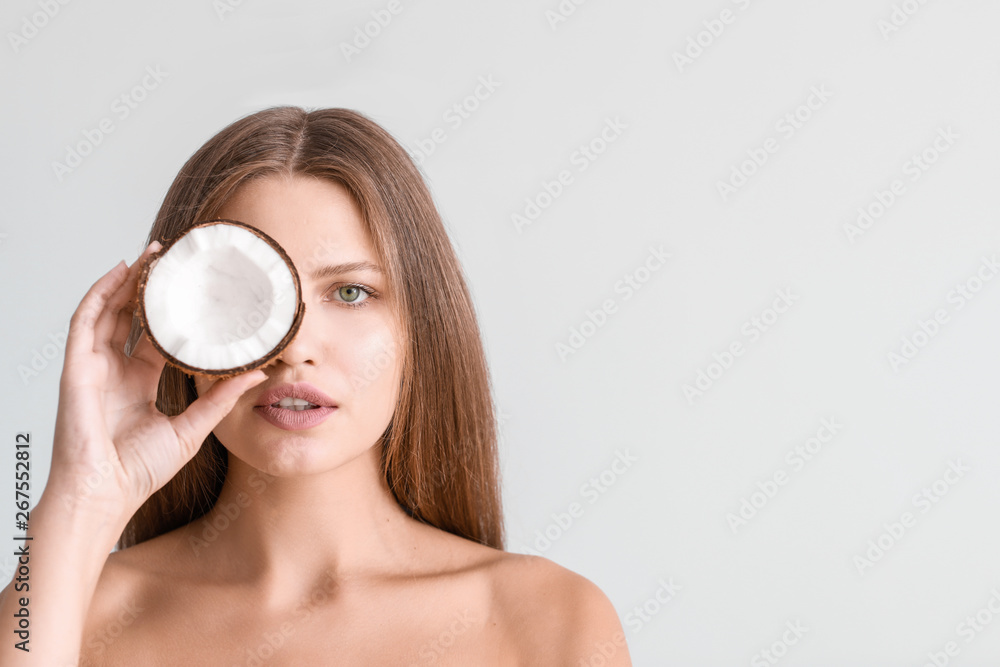 Beautiful young woman with coconut on light background