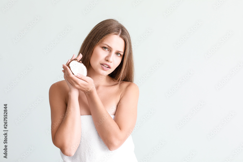 Beautiful young woman with coconut on light background