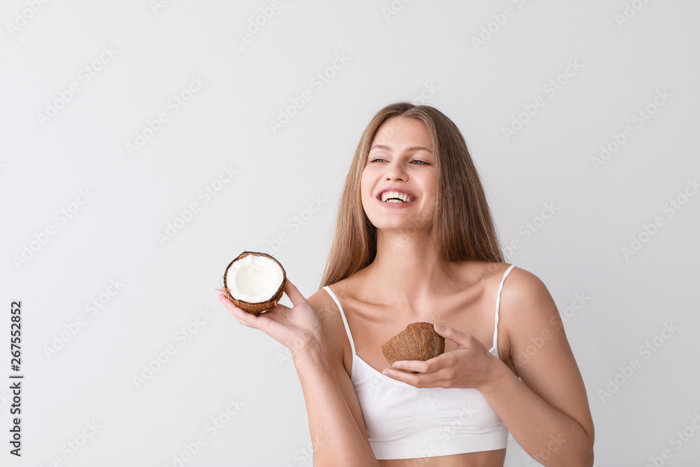 Beautiful young woman with coconut on light background