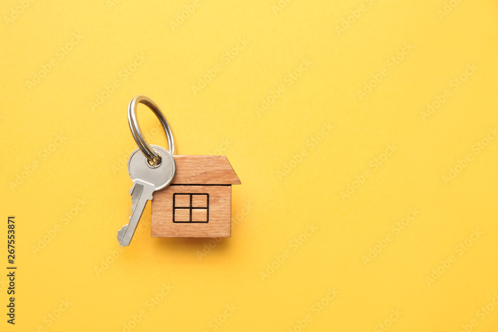 Key with trinket in shape of house on color background