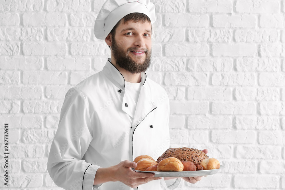 Young chef with fresh bakery products on white brick background