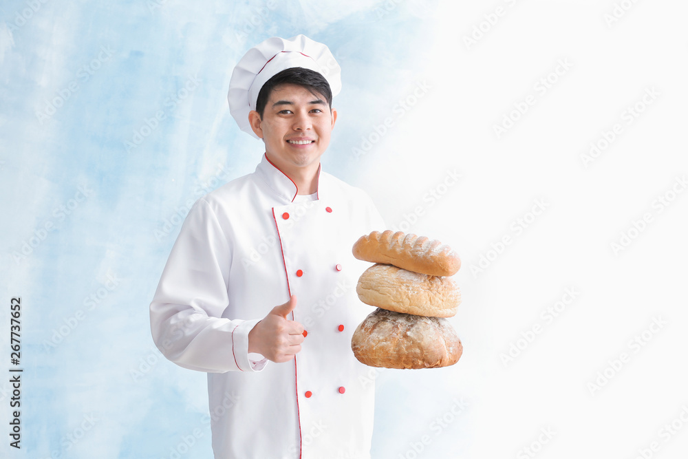 Asian baker with fresh bread showing thumb-up gesture on color background