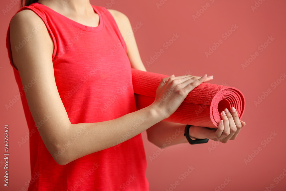 Young sporty woman with yoga mat on color background