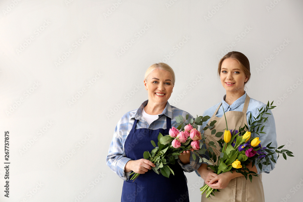 Female florists with bouquets on light background