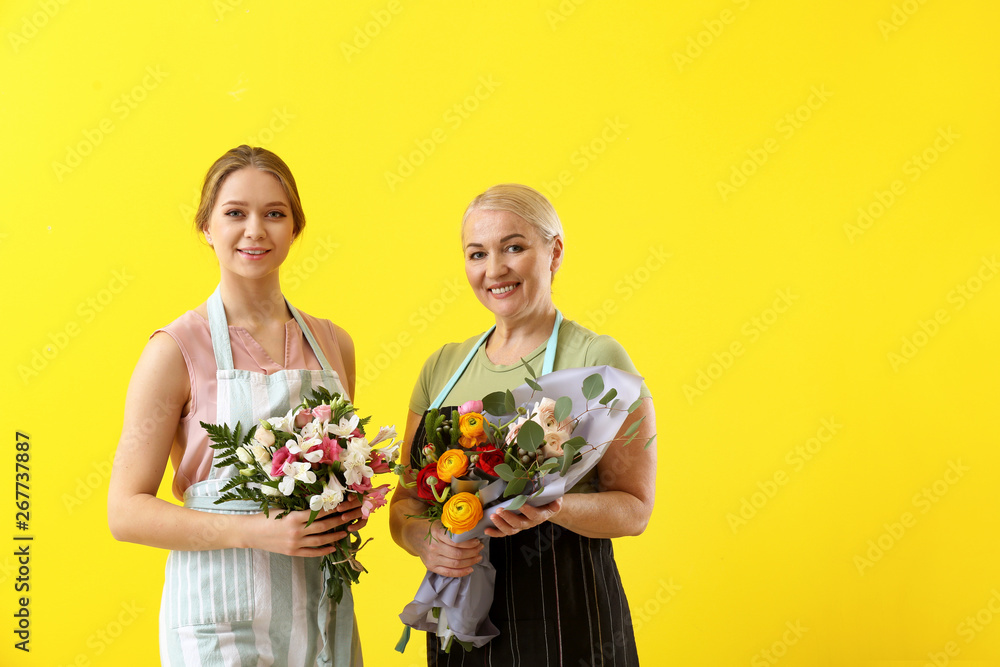 Female florists with bouquets on color background