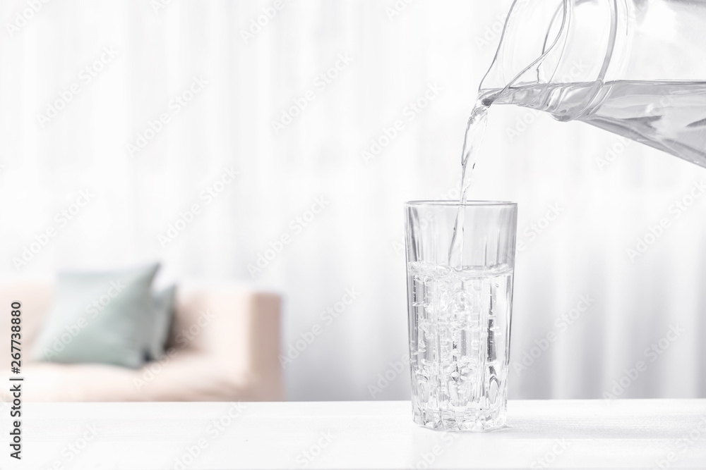 Pouring of fresh water into glass on table