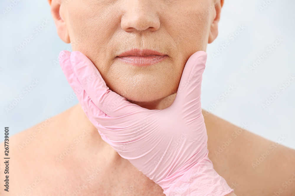 Plastic surgeon touching face of mature woman on light background, closeup