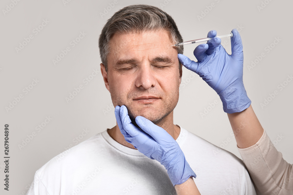 Mature man and hands holding syringe for anti-aging injections on grey background