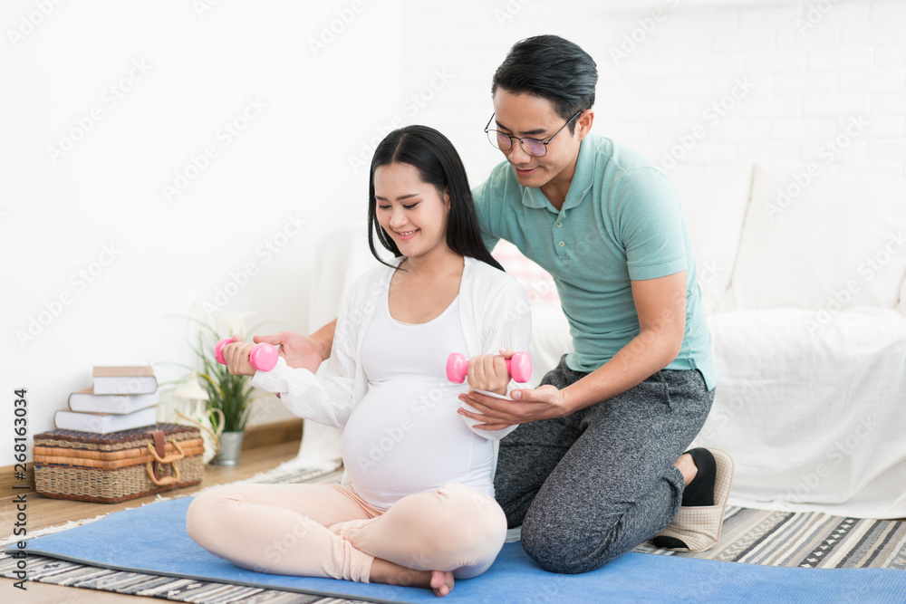 美丽的孕妇与丈夫一起用哑铃锻炼，在家帮助妻子，身体健康