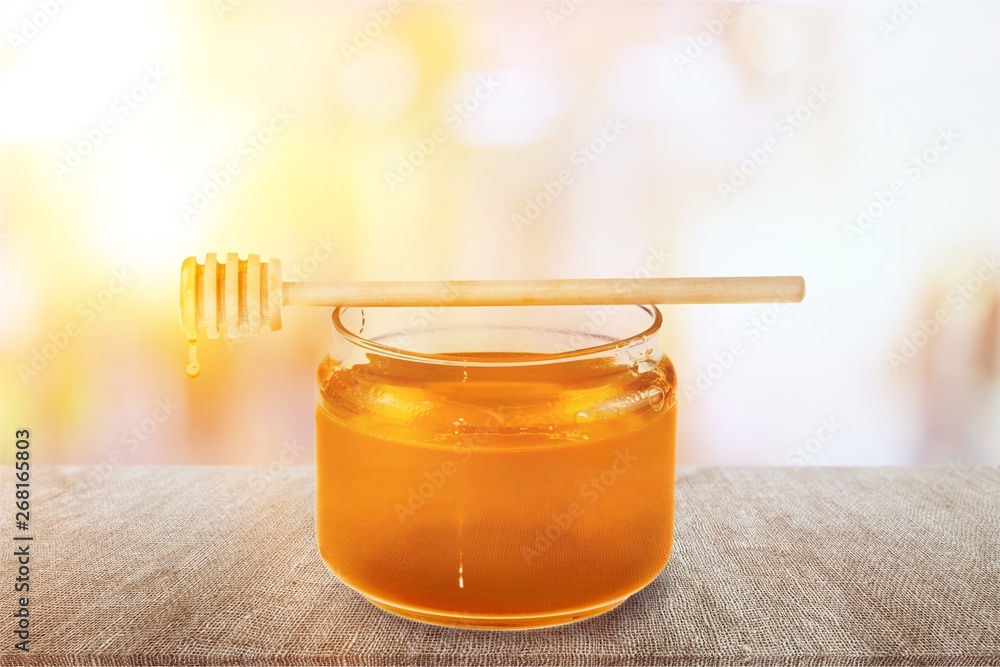 Fresh sweet honey with wooden honey dipper in glass jar isolated on white background