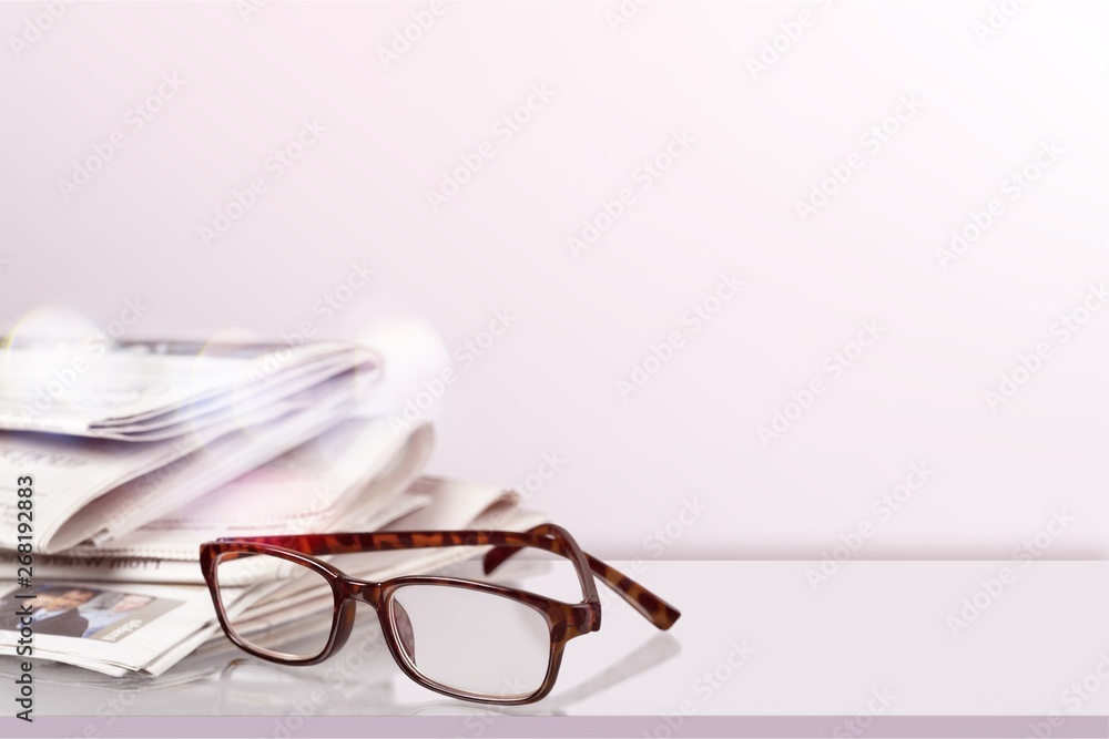 Newspapers with reading glasses on background