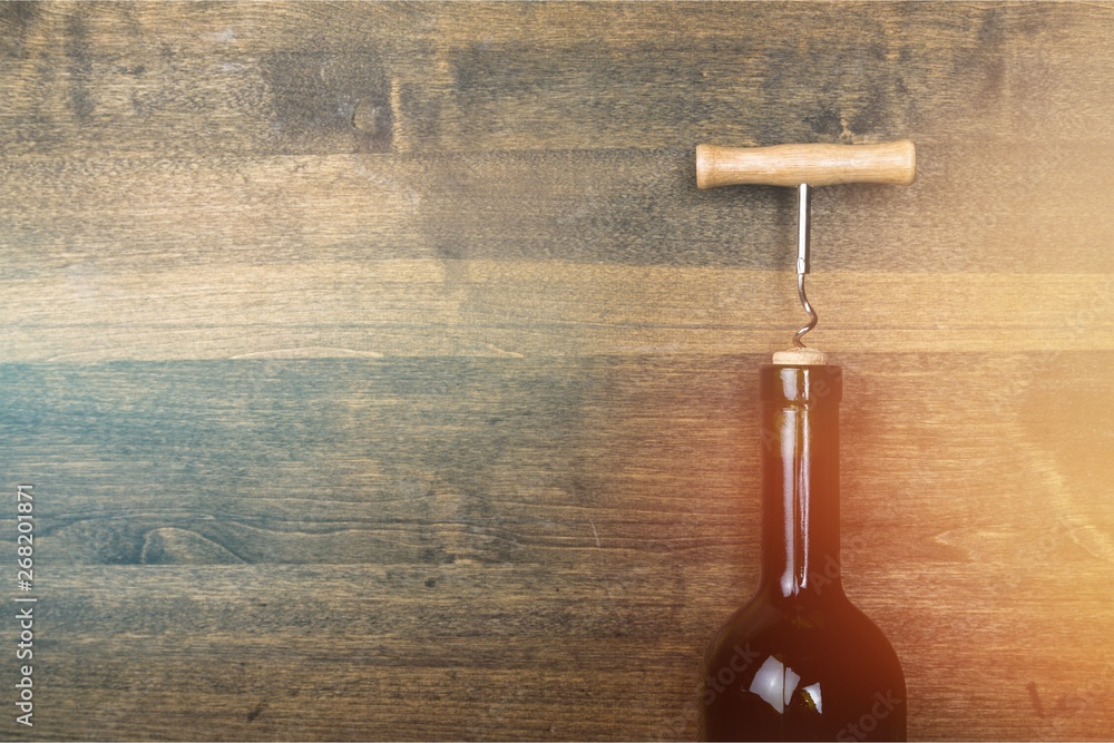 Bottle of wine with corkscrew on wooden background