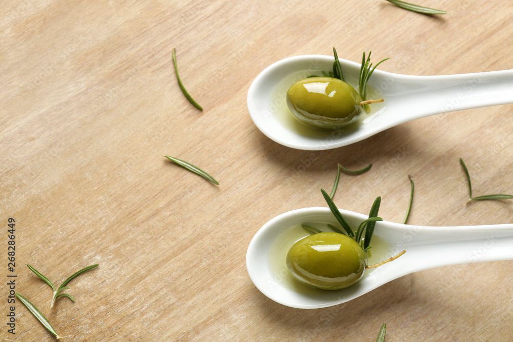 Spoons with olives on wooden board