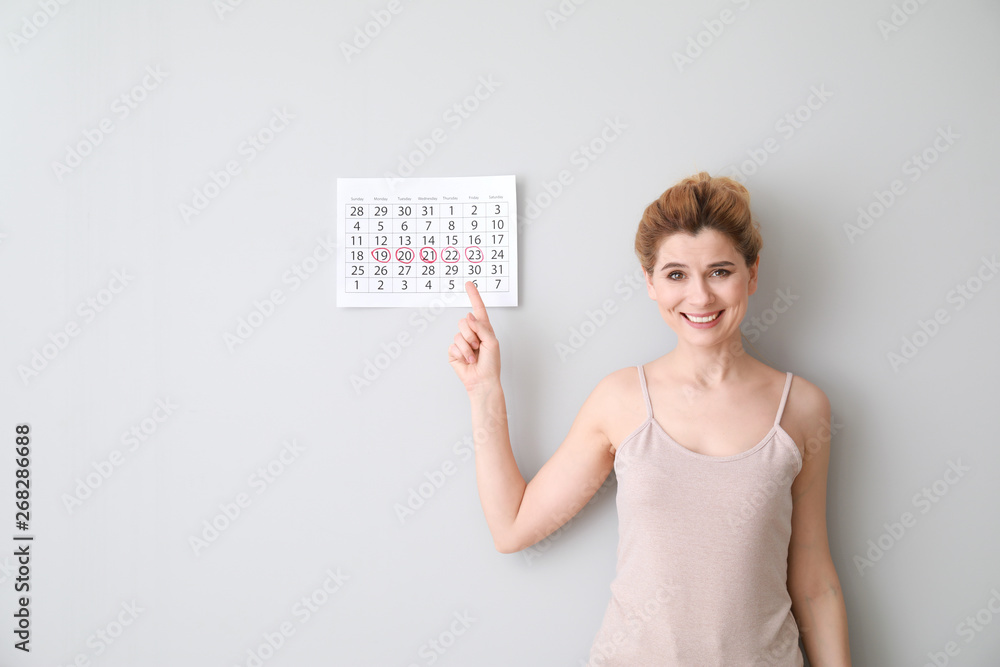 Happy woman with calendar on light background