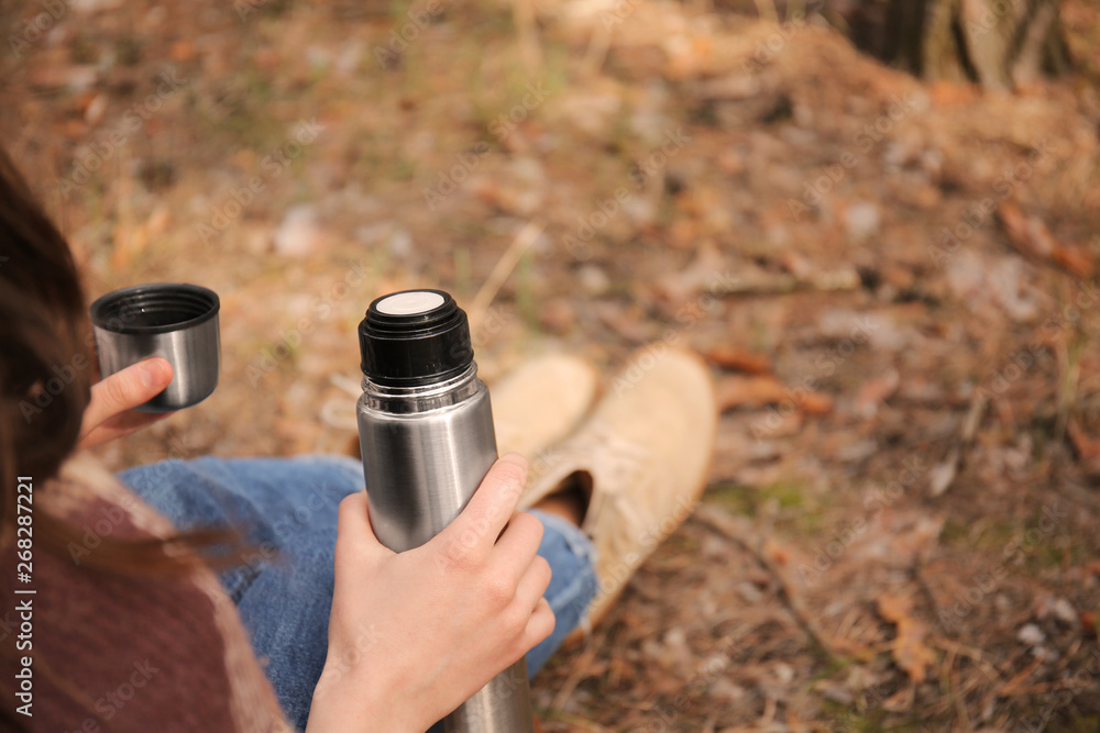 Woman drinking hot tea from thermos in forest