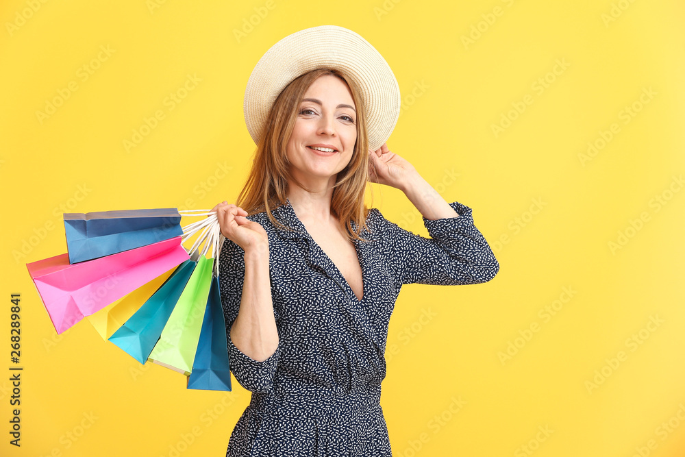 Portrait of mature woman with shopping bags on color background