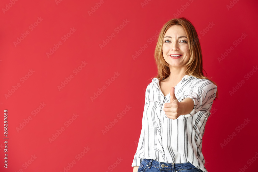 Portrait of mature woman showing thumb-up on color background