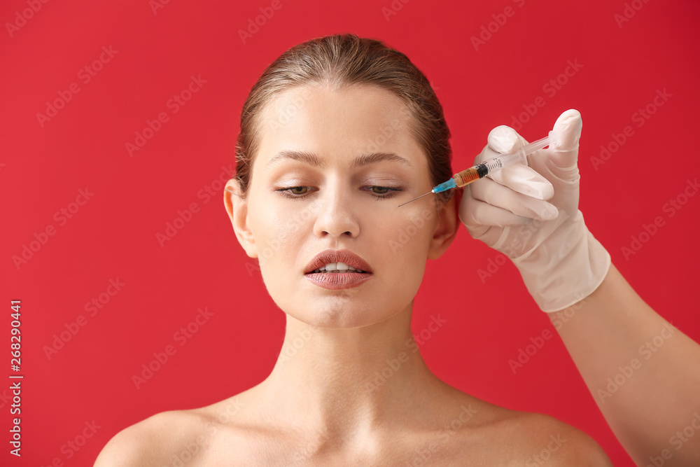 Hand of plastic surgeon with syringe and young woman against color background