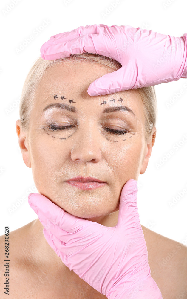 Plastic surgeon touching face of mature woman with applied marks on white background