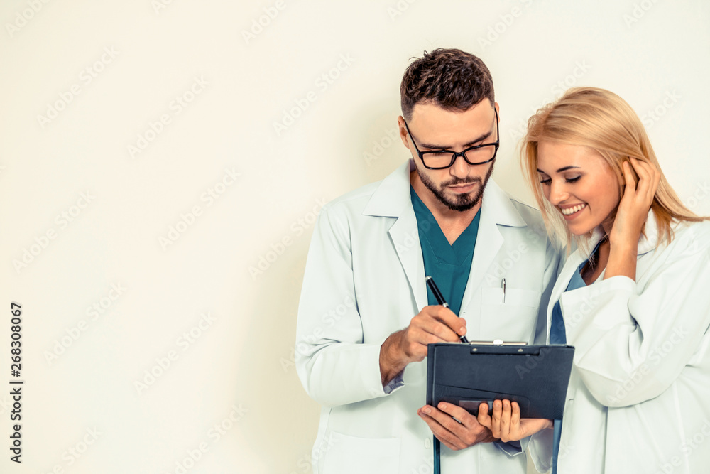 GP doctor looks at data in documents on clipboard while discussing with surgical doctor on white bac