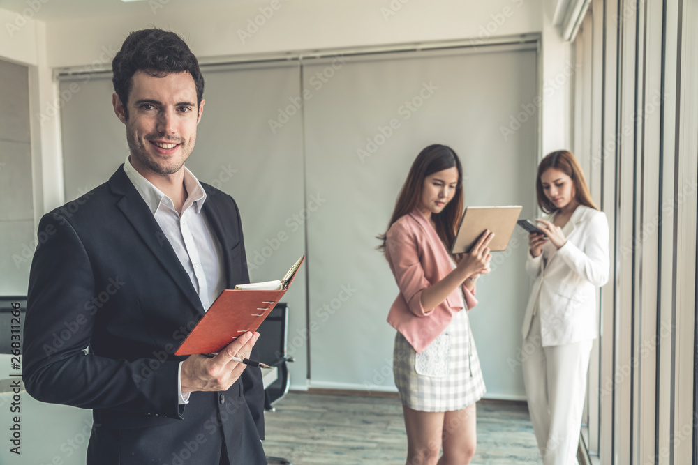 Happy young handsome businessman reading book and working in office with colleagues and friend at wo