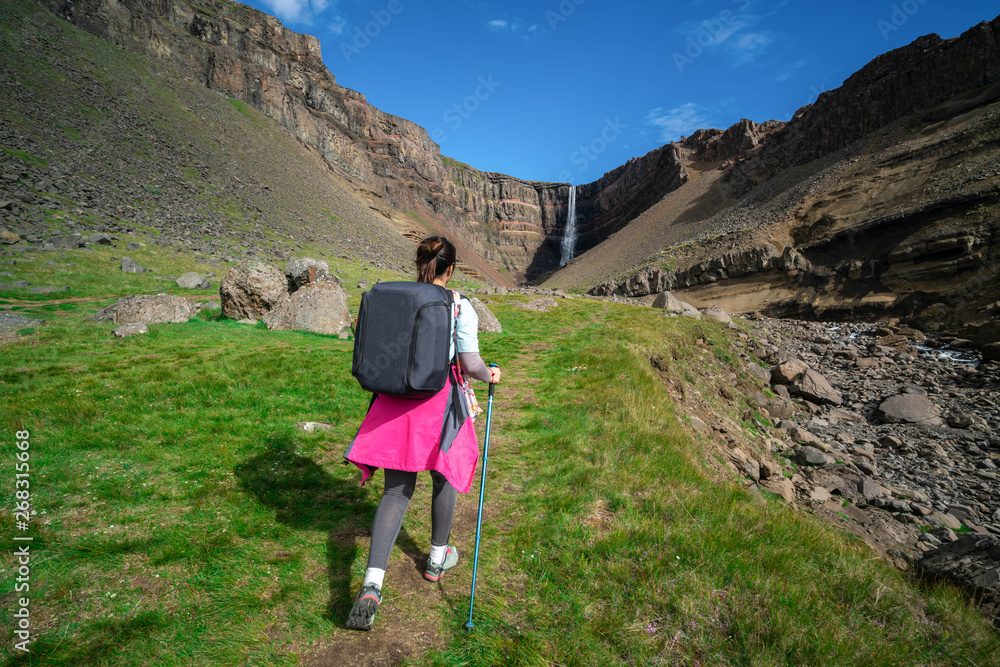 Woman traveler trekking in Icelandic summer landscape at the Hengifoss waterfall in Iceland. The wat