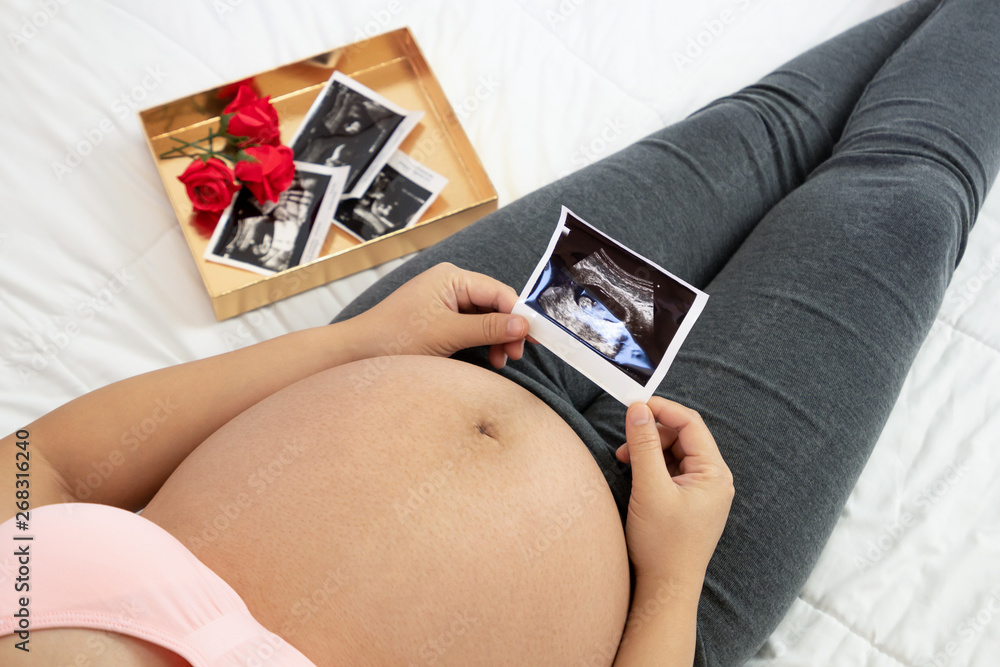 Pregnant woman feeling happy at home while taking care of her child. The young expecting mother hold