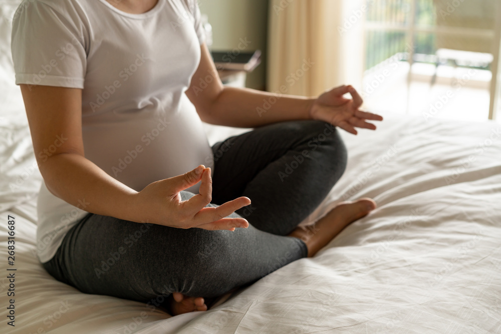 Pregnant woman doing yoga exercise on bed in bedroom at home while taking care of her child. The hap