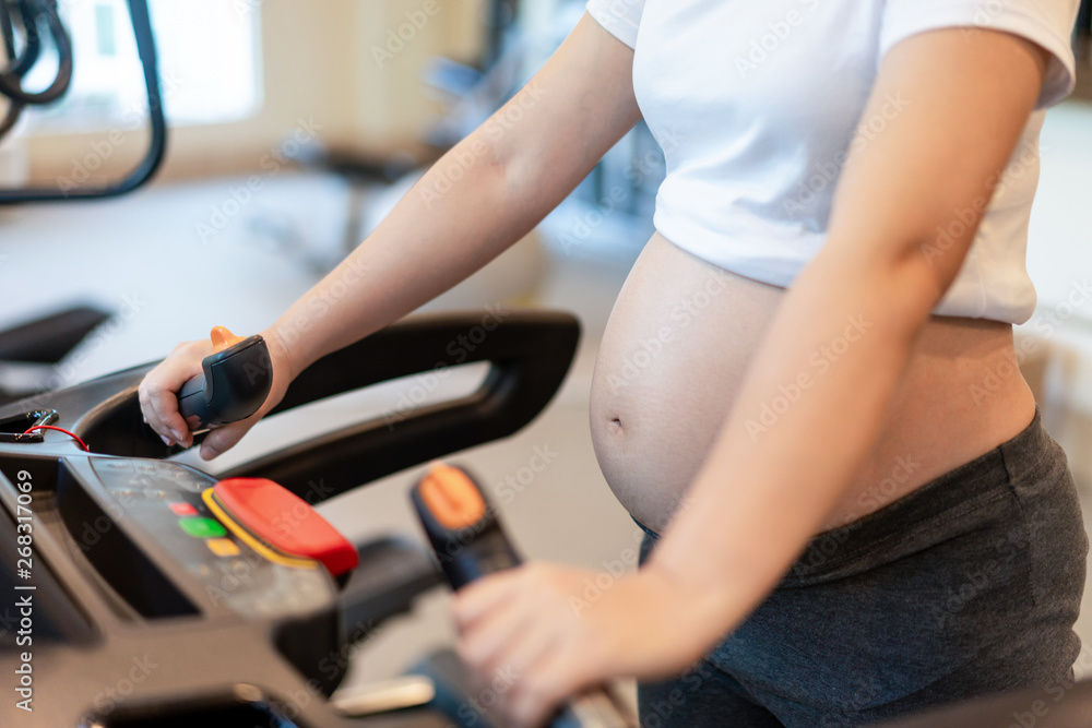 Active pregnant woman exercise in fitness center at yoga room. The young expecting mother holding ba