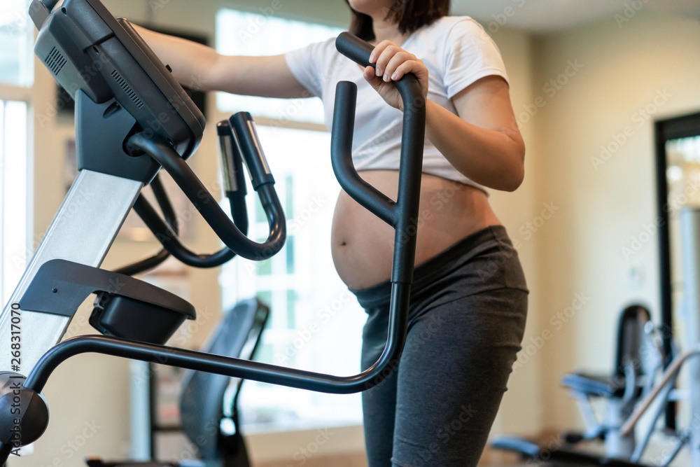 Active pregnant woman exercise in fitness center at yoga room. The young expecting mother holding ba