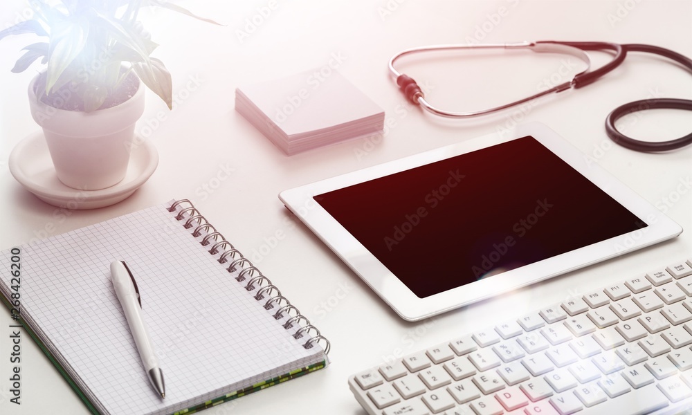 Digital tablet with green plant, pen, notebook and stethoscope on table in office