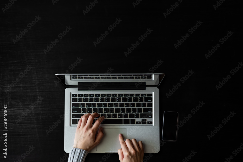  top view of hand working with laptop computer, smartphone, tablet, coffee cup, pen, notepad on  dar