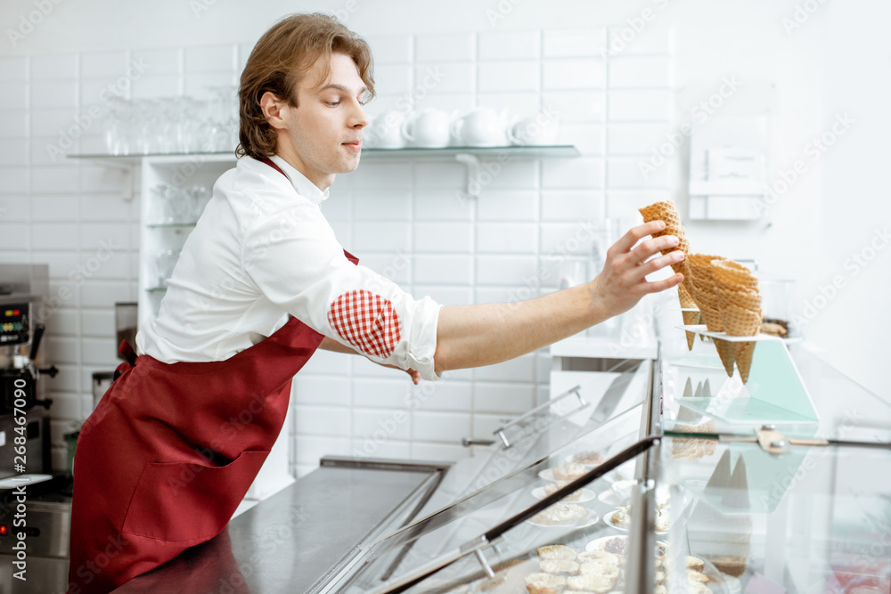 英俊的推销员在现代糕点店为客户做冰淇淋时拿着华夫饼蛋卷