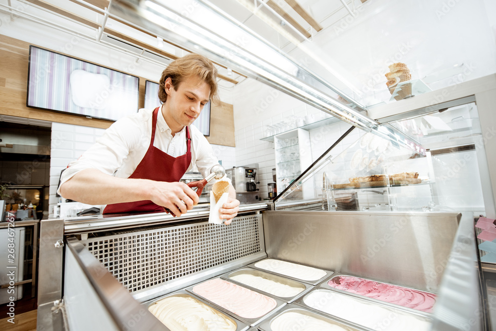 Salesman taking ice cream from the trays on the showcase refrigerator and putting into the waffle co