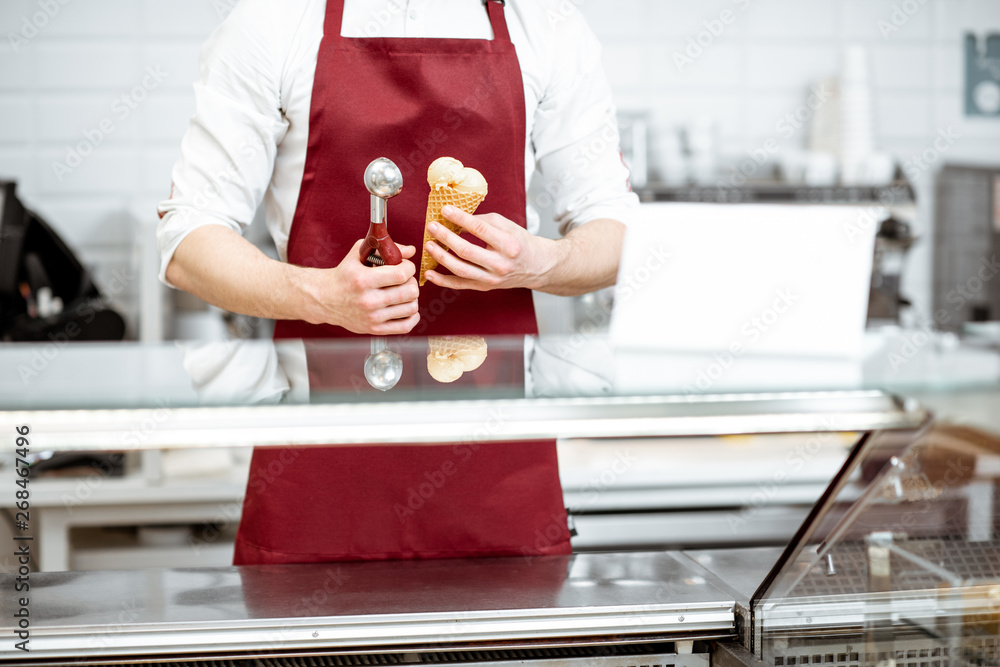 推销员拿着华夫饼蛋卷里的冰淇淋，红色围裙背景上的专业勺子，cl