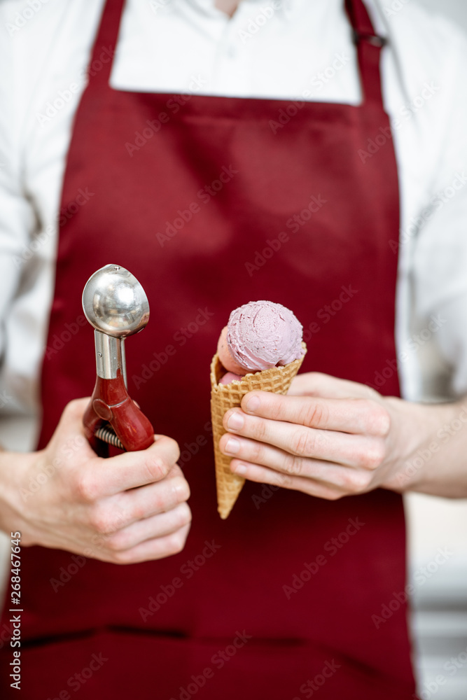 推销员拿着华夫饼蛋卷里的冰淇淋，红色围裙背景上的专业勺子，cl