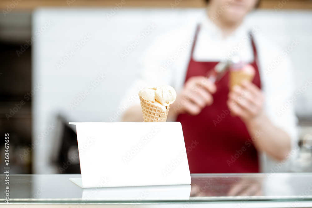 Ice cream in the waffle cone on the counter of the pastry shop with salesperson on the background