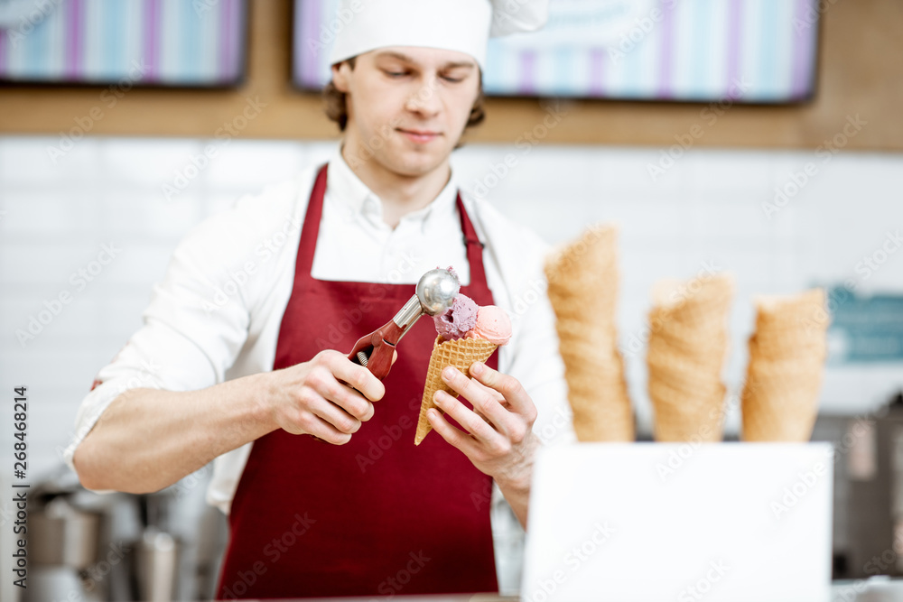 现代糕点店的年轻推销员，穿着围裙，戴着帽子，用华夫饼做冰淇淋