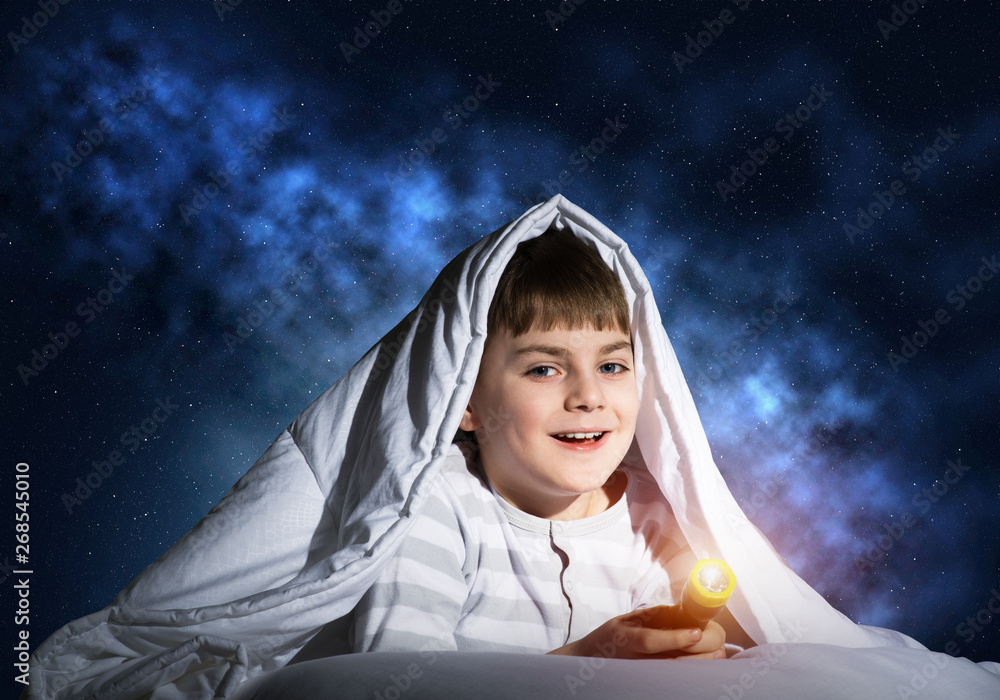 Happy child with flashlight hiding under blanket