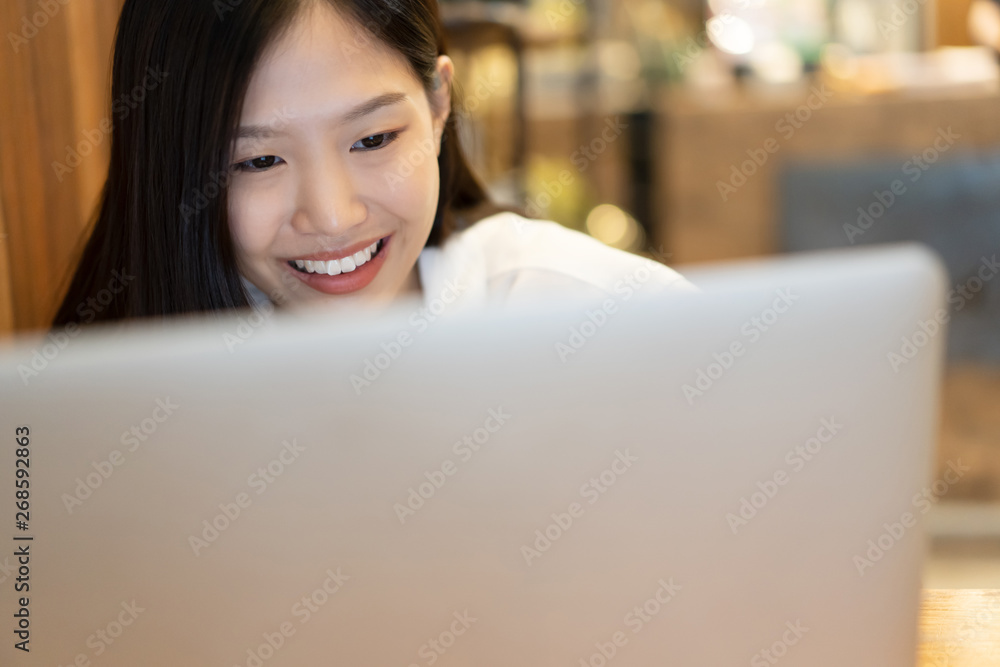 Happy young Asian woman using phone and working with a laptop in the coffee shop cafe office.