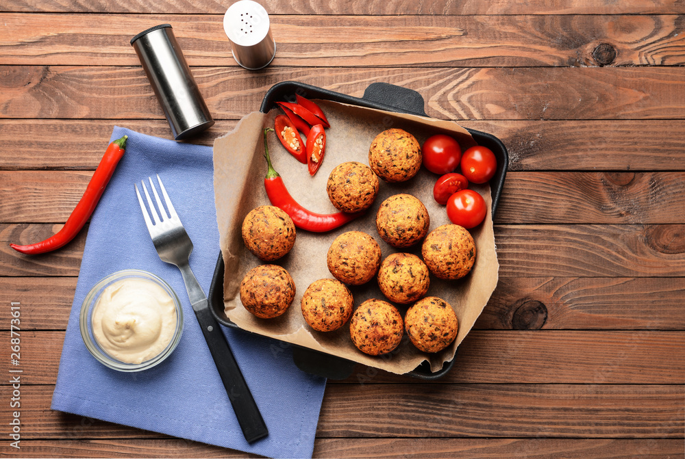 Frying pan with tasty falafel balls and sauce on wooden table