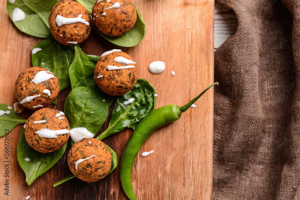 Tasty falafel balls with chili and spinach on wooden board