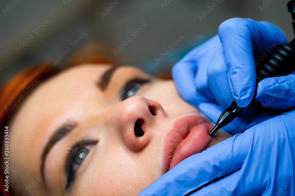 Permanent make-up for pink lips of beautiful woman in beauty salon. Beautician doing tattooing lips.