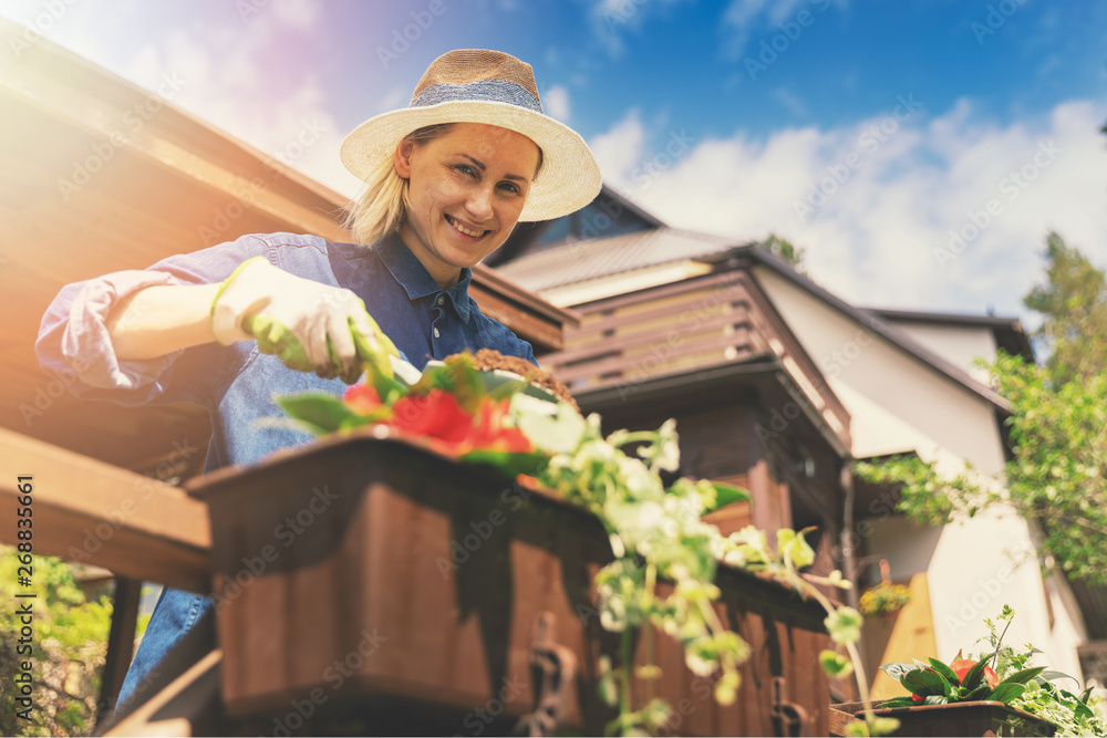 smiling young woman planting flowers in boxes on patio railings