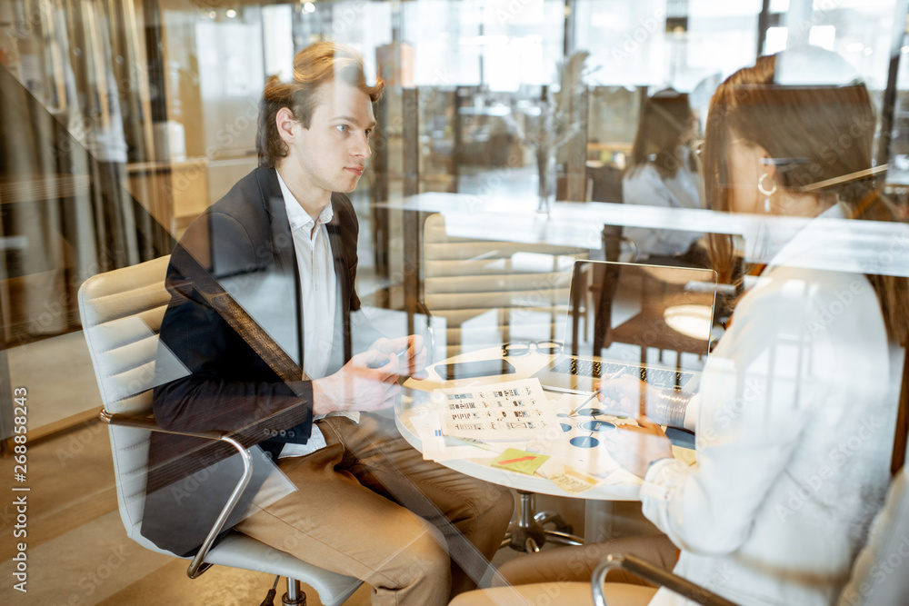 Business man and woman having a conversation in the meeting room, view through the glass partition w