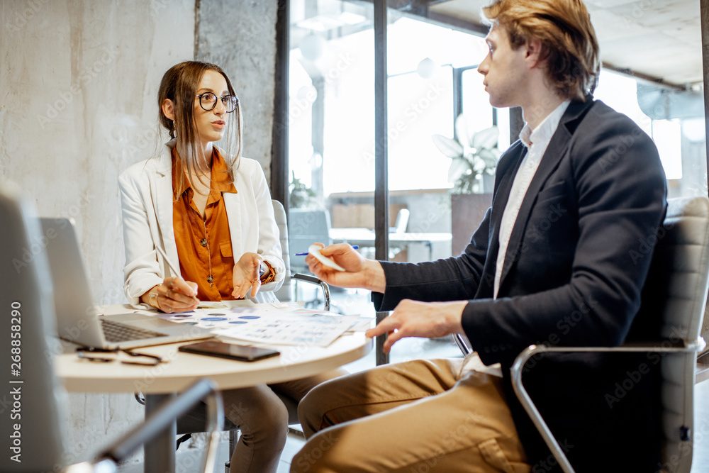 Young man and woman having a serious business conversation, working with paper documents and compute