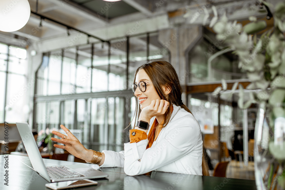 Portrait of a young and cheerful business woman sitting with laptop a the modern spacious bar or off