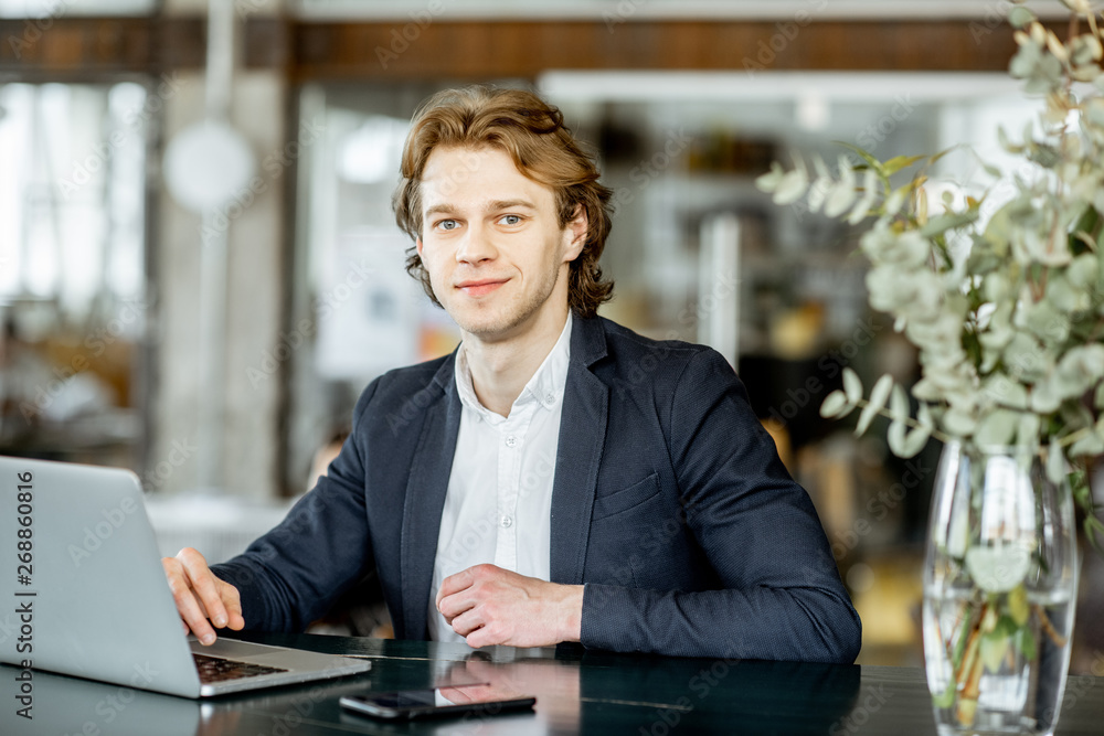 Portrait of a young handsome businessman sitting with laptop at the modern spacious bar or office