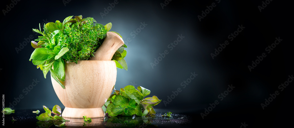 Herbs. Bunch of Fresh green organic aromatic herb leaves in wooden mortar with pestle over black bac