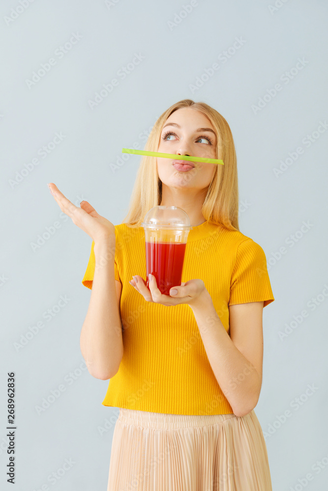 Funny young woman with fresh juice on light background